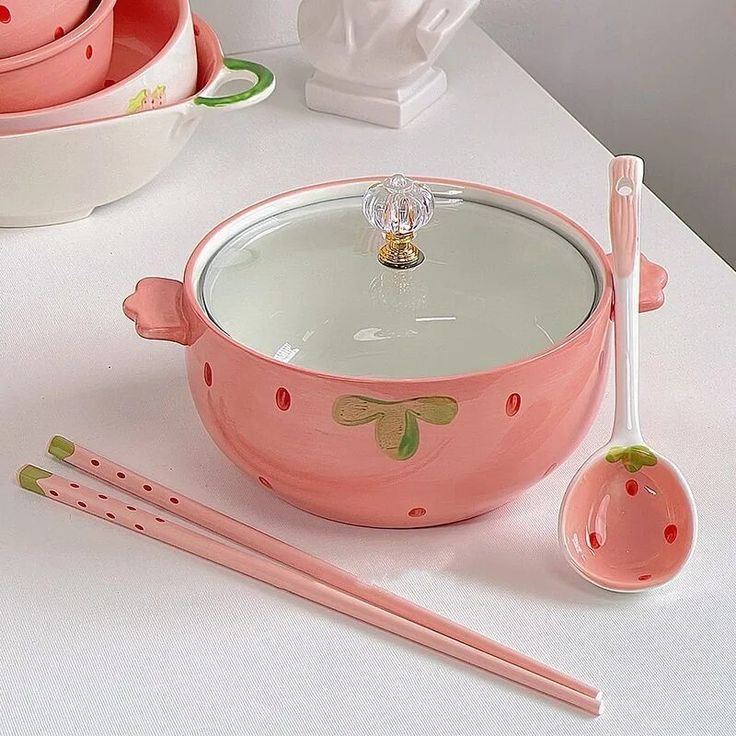 a pink bowl with spoons and utensils on a white table