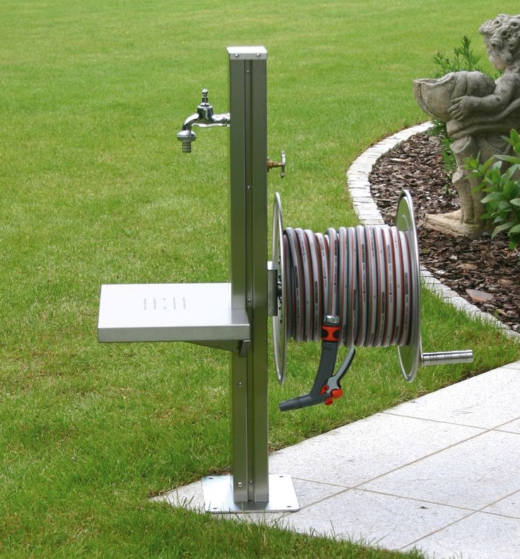 a garden hose dispenser in the middle of a grassy area next to a statue