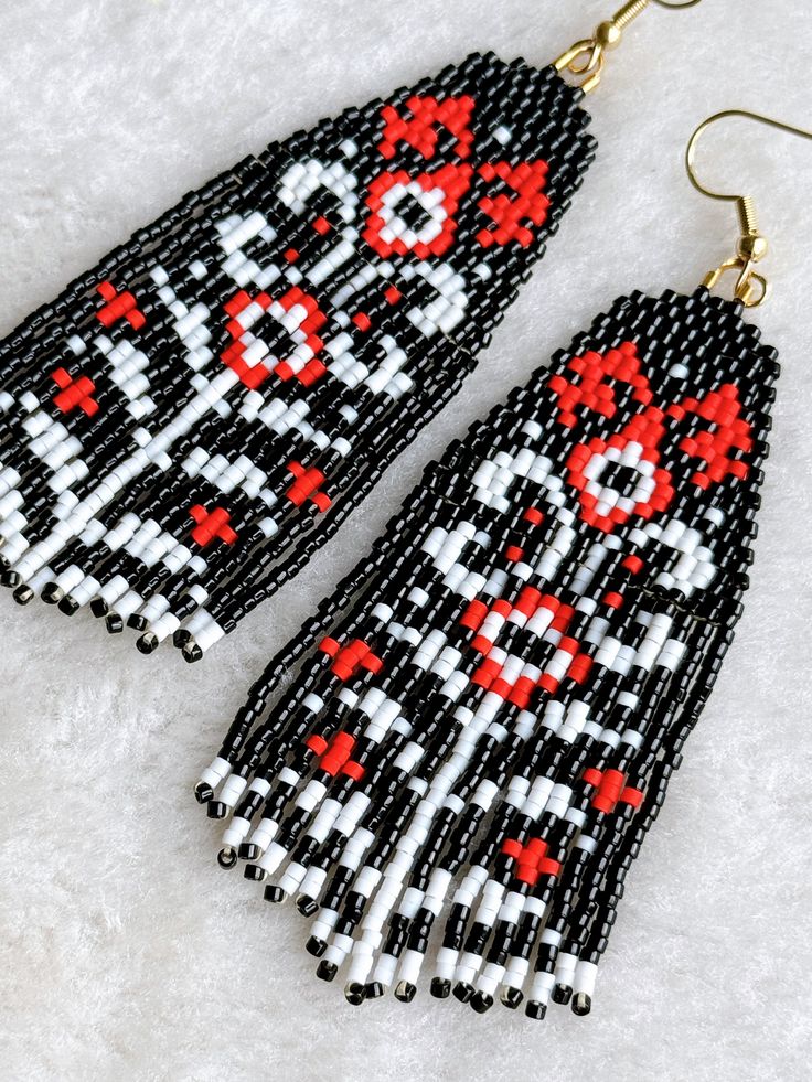 black and white beaded earrings with red cross stitching on the ends, hanging from gold earwires