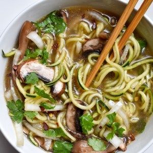 a bowl filled with noodles, mushrooms and cilantros next to chopsticks