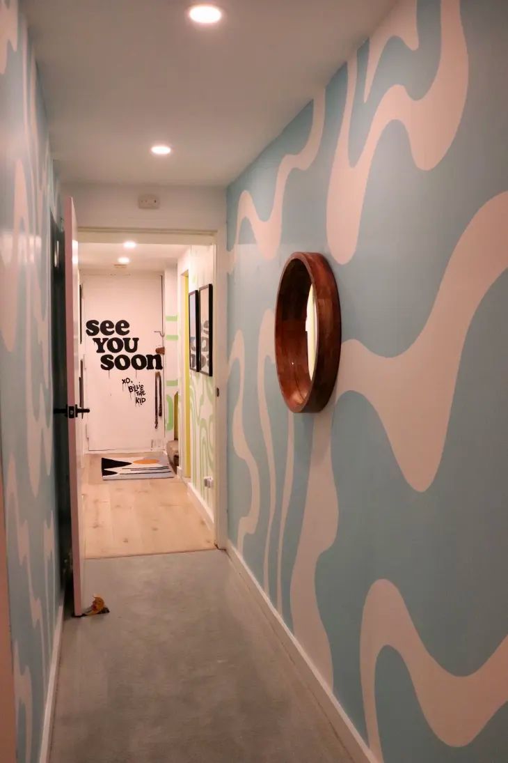 an empty hallway with blue and white wallpaper on the walls, and a round mirror hanging on the wall