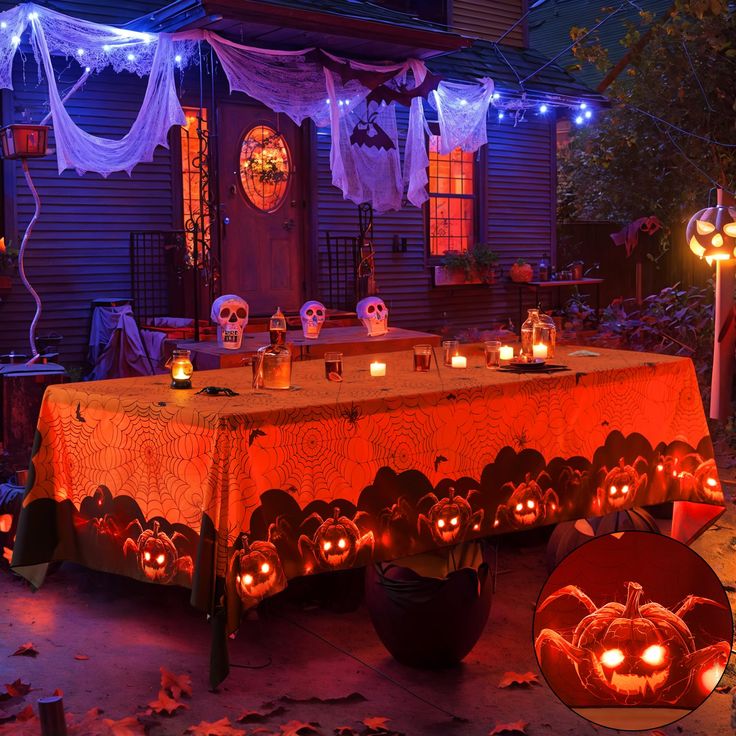 a table covered with pumpkins and candles in front of a house decorated for halloween