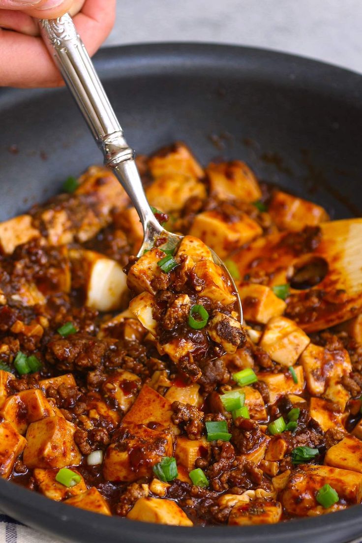 someone is spooning food out of a pan with meat and green onions on it