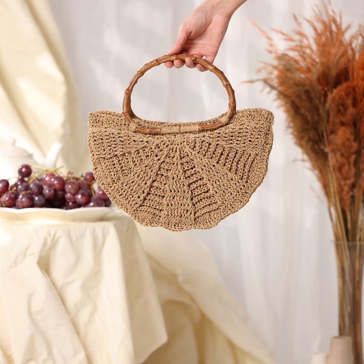 a hand holding a woven purse next to a vase with dried red grapes in it