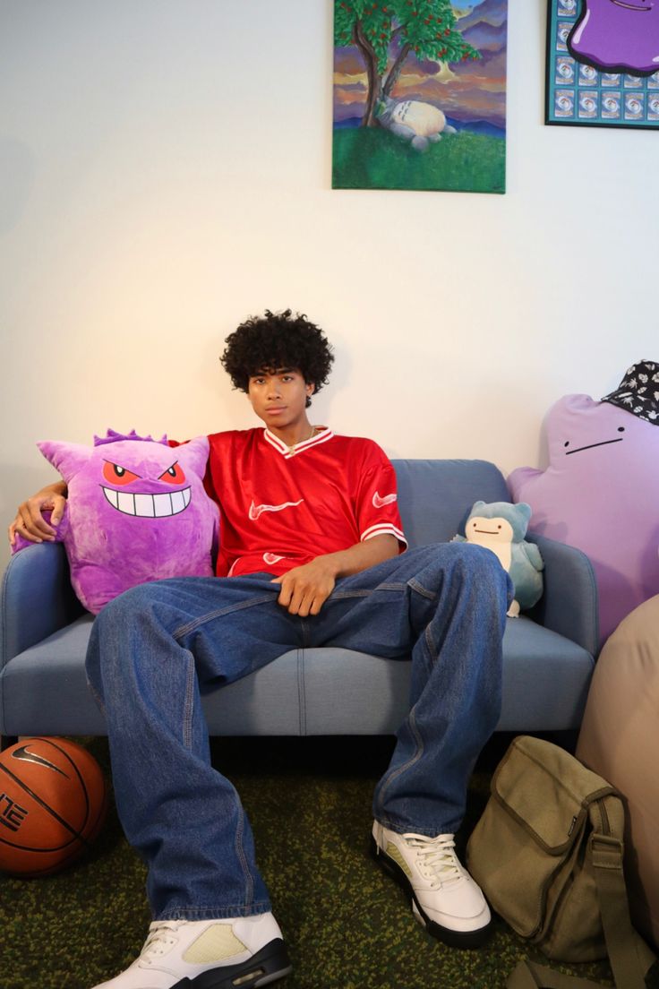 a man sitting on top of a blue couch next to two stuffed animals and a basketball