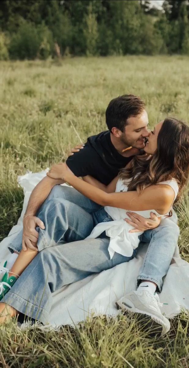 a man and woman sitting in the grass kissing