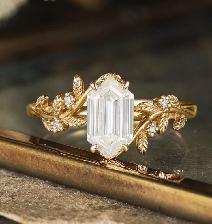 a close up of a gold ring with an emerald stone and leaves on the side