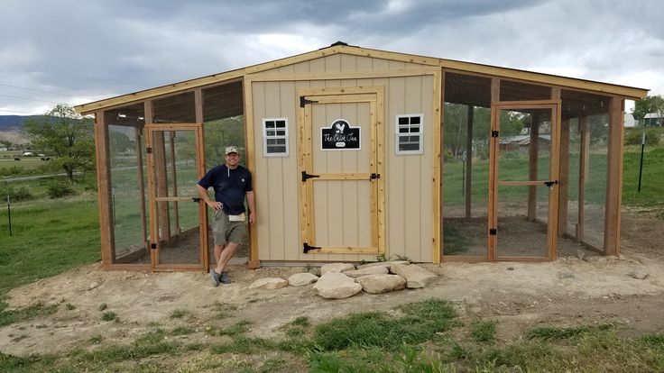 a man standing in front of a chicken coop on the side of a field with rocks and grass