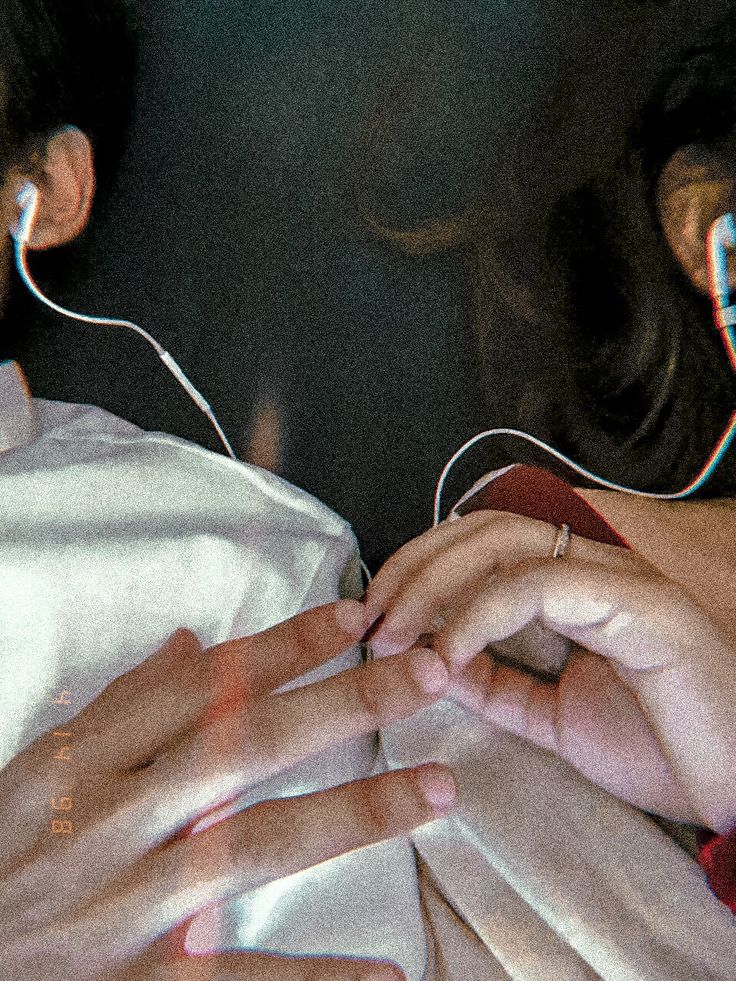 two people laying in bed with headphones on their ears and hands touching each other