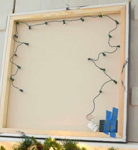 a white board with string lights hanging from it's sides and some pine branches in front of it