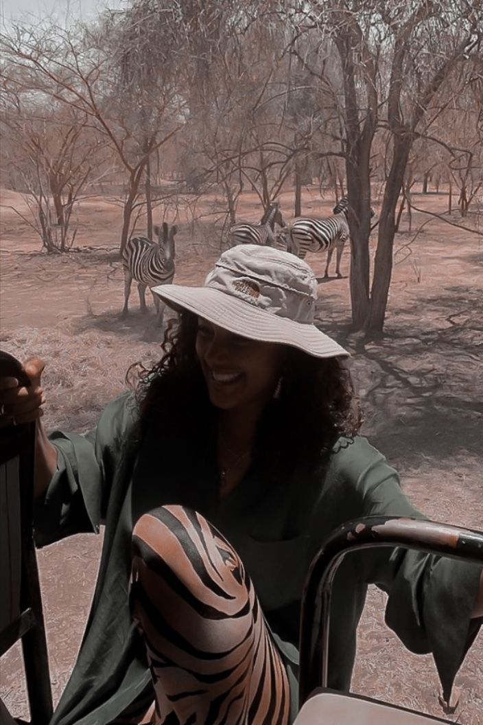 a woman sitting in the drivers seat of a vehicle with zebras behind her and trees