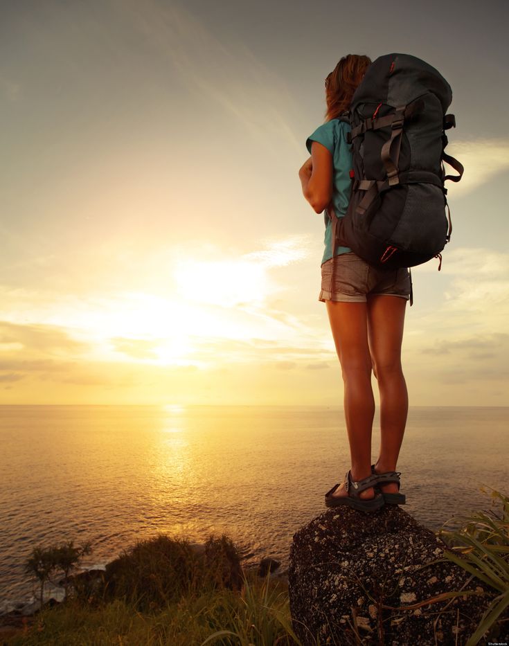 a woman standing on top of a cliff overlooking the ocean at sunset with her back to the camera