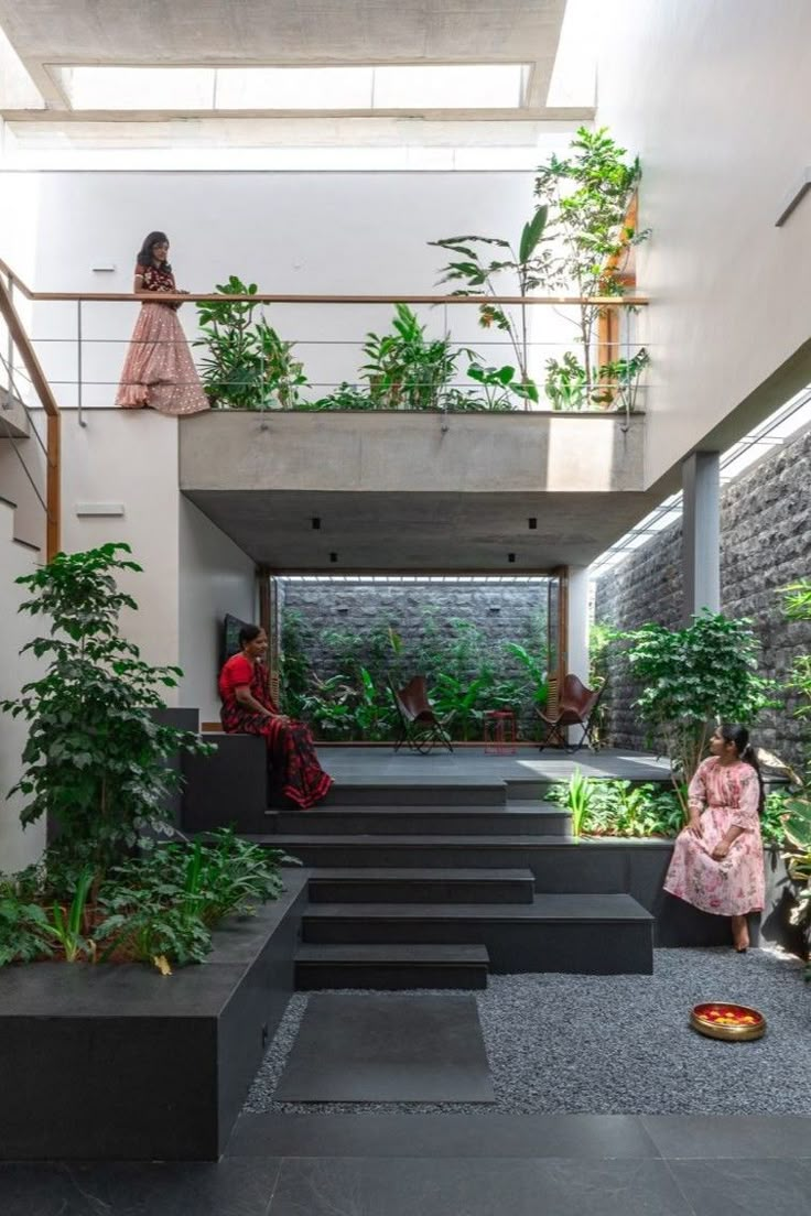 two women are sitting on the stairs in an indoor space with plants and other greenery