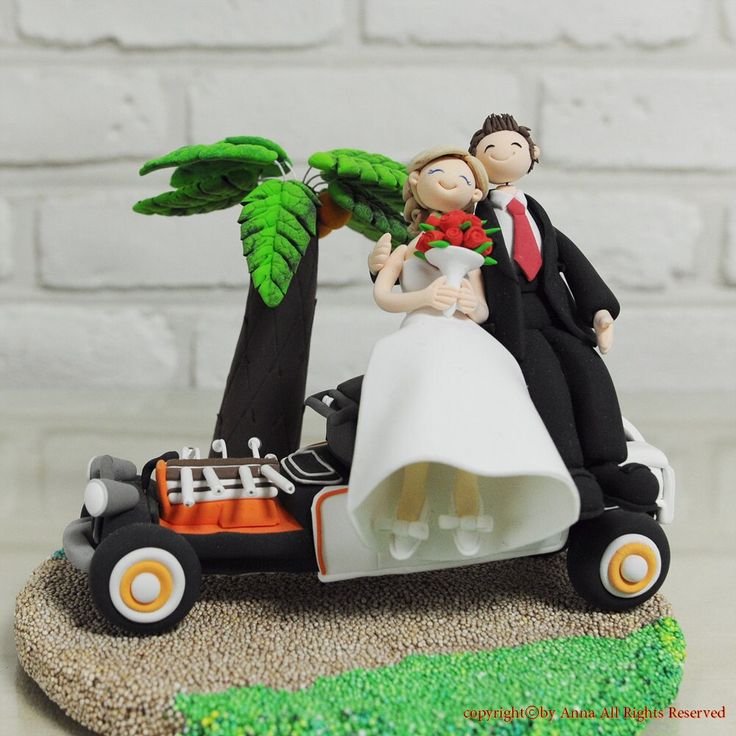 a wedding cake topper with a bride and groom in a race car on the beach