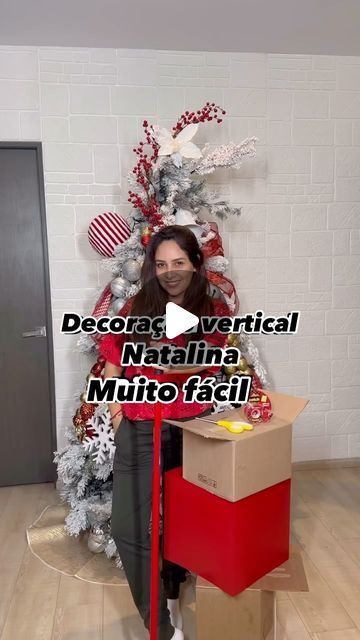 a woman standing in front of a christmas tree holding a box with decorations on it