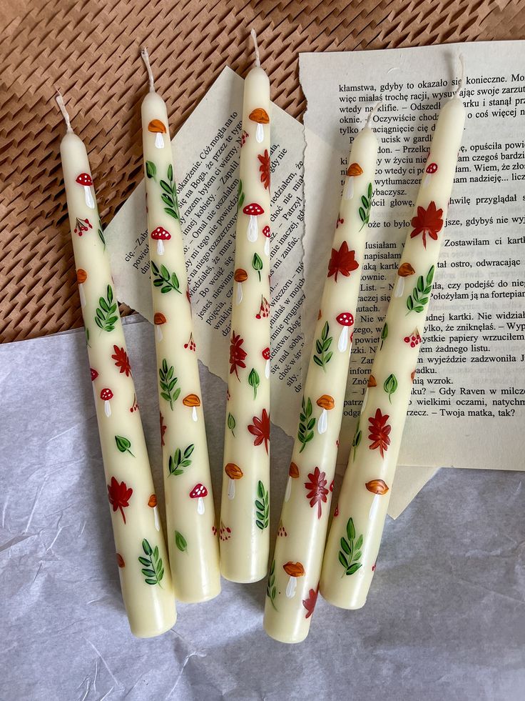 four candles sitting on top of a table next to an open book with leaves painted on them