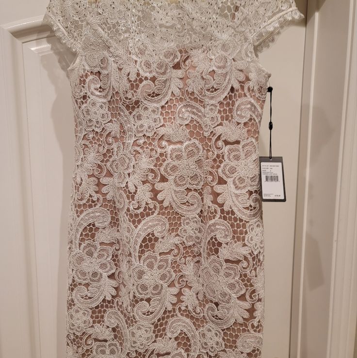 a white lace dress hanging on a door with a tag attached to the back of it