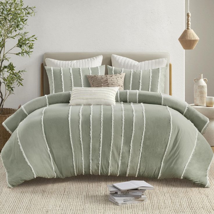 a bed with green comforter and pillows in a room next to a potted plant