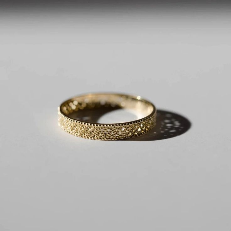 a yellow gold wedding ring on a white surface with the shadow from it's side