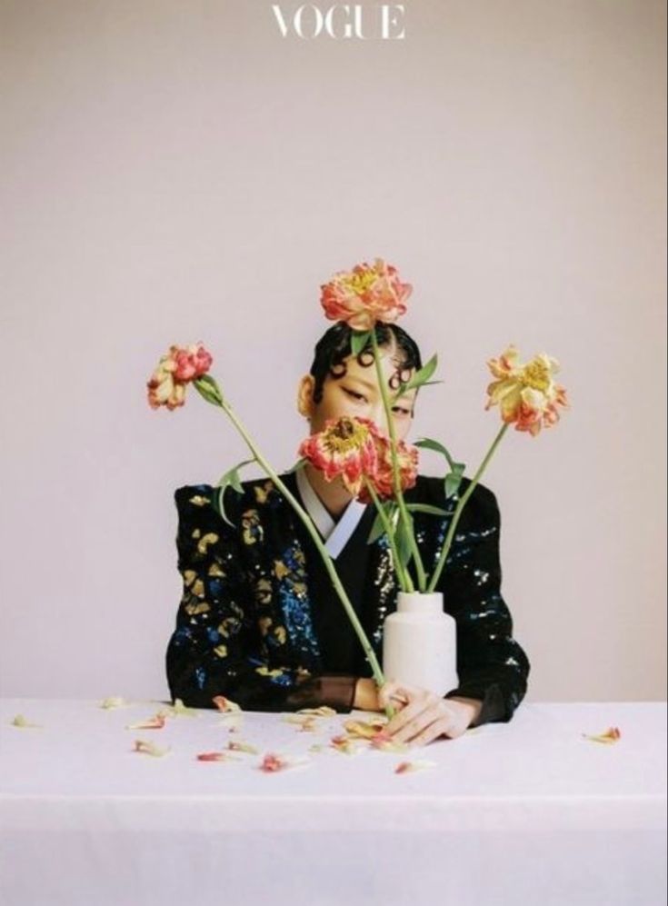 a woman sitting at a table with flowers in front of her face and the words voge on it