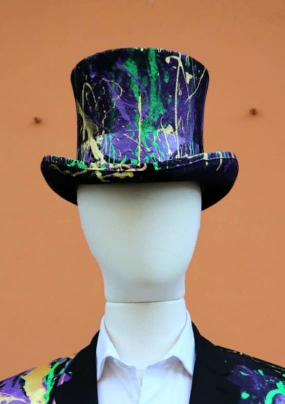 a white mannequin wearing a colorful suit and top hat with paint splattered on it