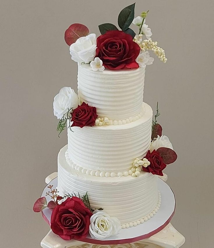 a three tiered white wedding cake with red and white flowers