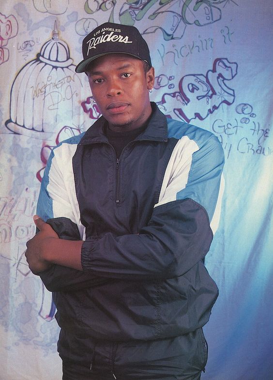 a man standing in front of a graffiti covered wall with his arms crossed and looking at the camera