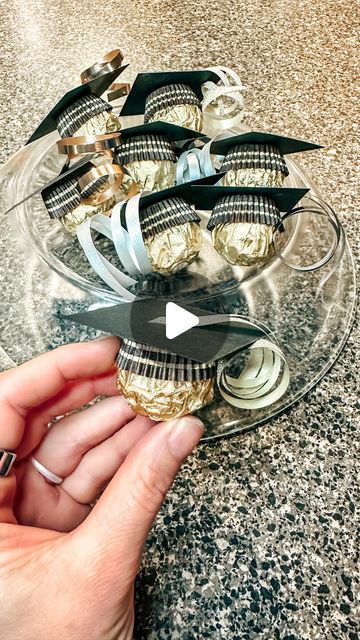 a person is holding a glass plate with gold and black pins in it, which are on top of a marble countertop