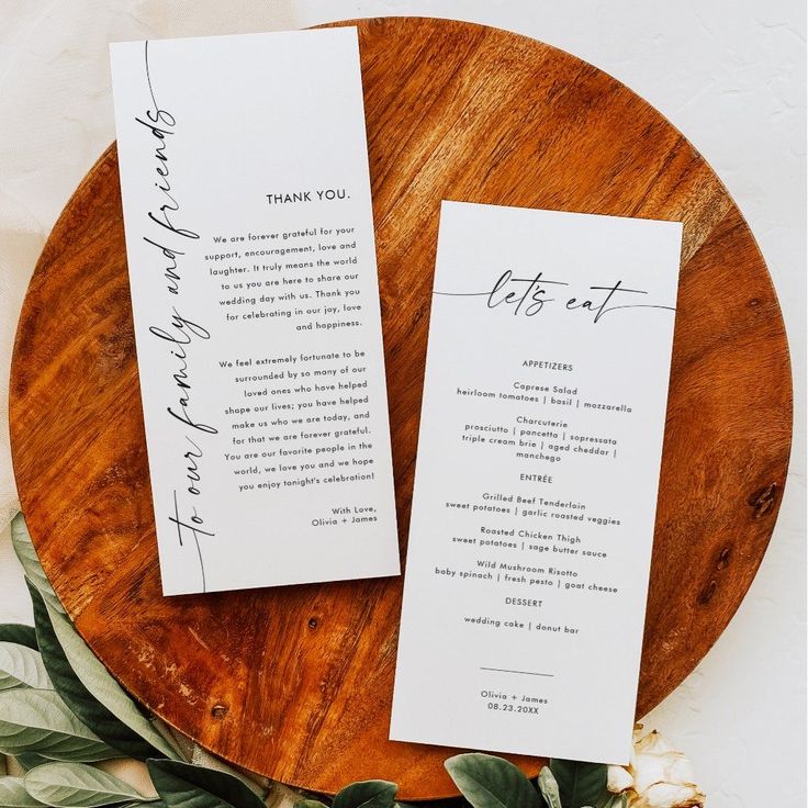 two wedding programs on a wooden plate with greenery