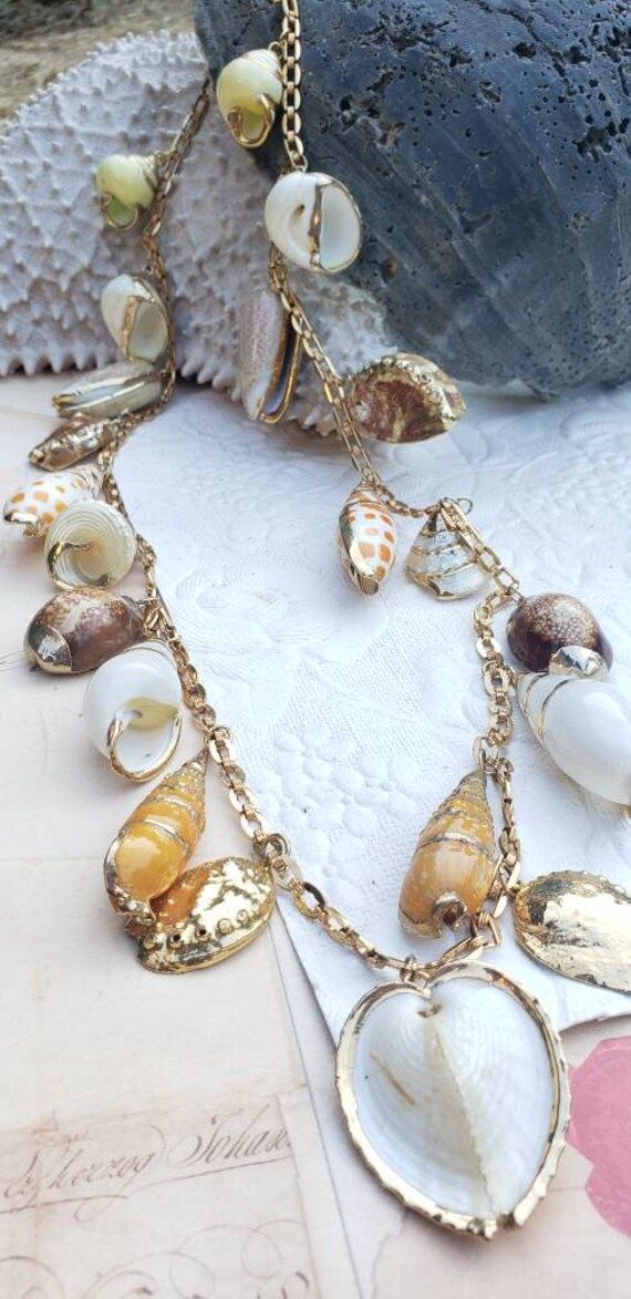 21 shells beautifully metal rimmed; Roget signed vintage necklace; 32 inches long; matching bracelet available. Bohemian Metal Shell Jewelry, Vintage Gold Shell Jewelry, Vintage Long Necklace Jewelry For Beach, Vintage Gold Beach Jewelry, Vintage Gold Jewelry For Beach, Vintage Gold Jewelry For The Beach, Handmade Vintage Gold Shell Necklace, Gold Shell-shaped Bohemian Necklace, Handmade Vintage Shell Necklace