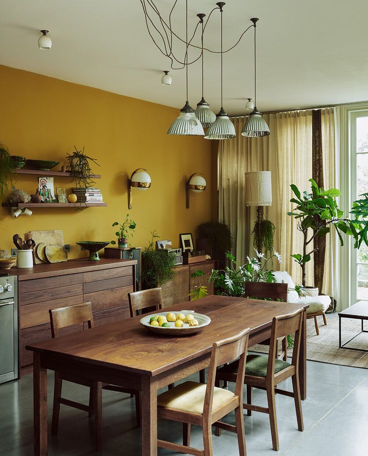 a dining room with yellow walls and wooden table surrounded by chairs, potted plants and hanging lights