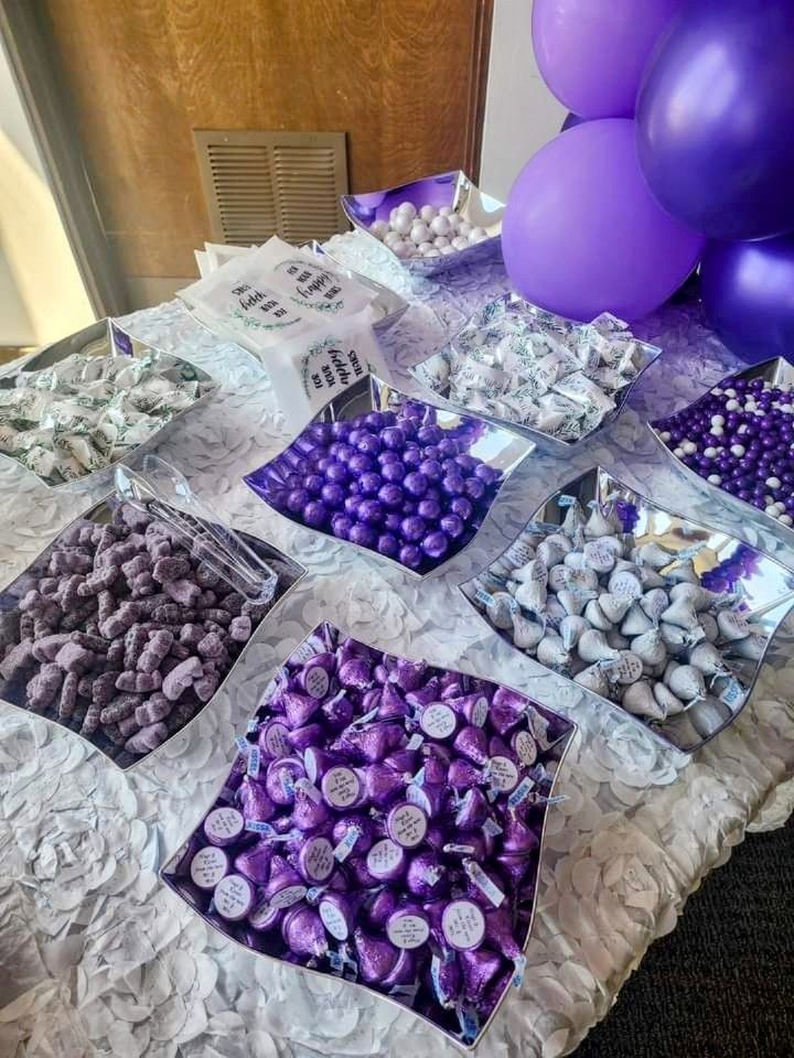 there are many purple and white candies on the table with balloons in the background