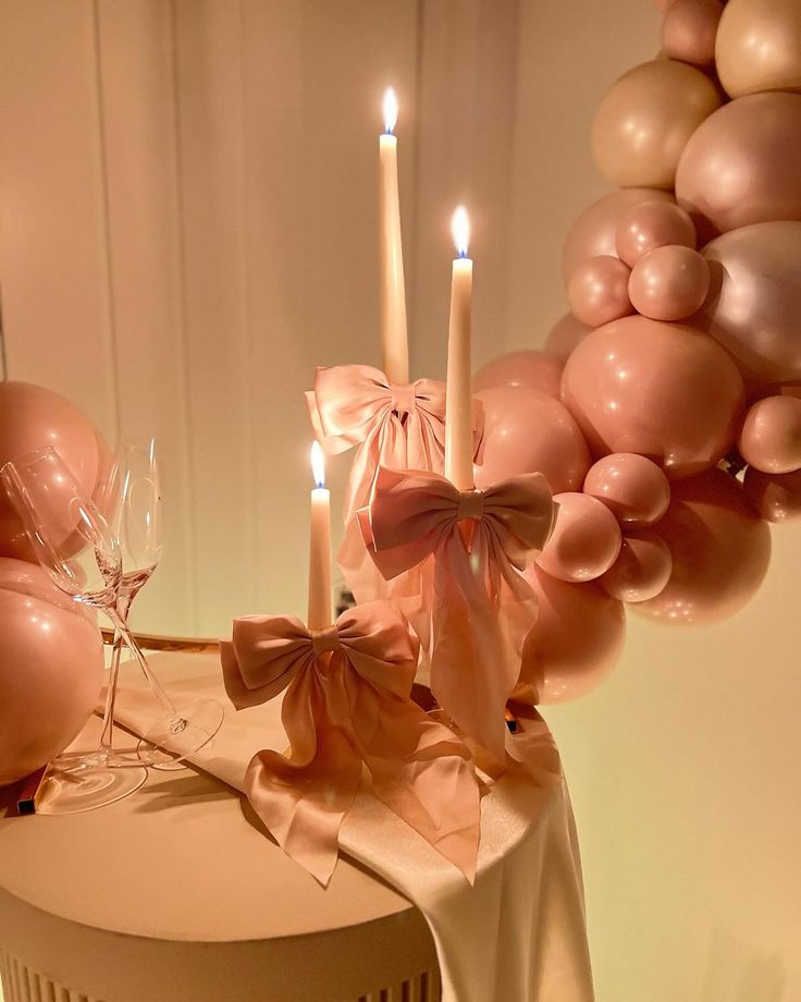 a table topped with balloons and candles next to a cake covered in pink ribbon bows