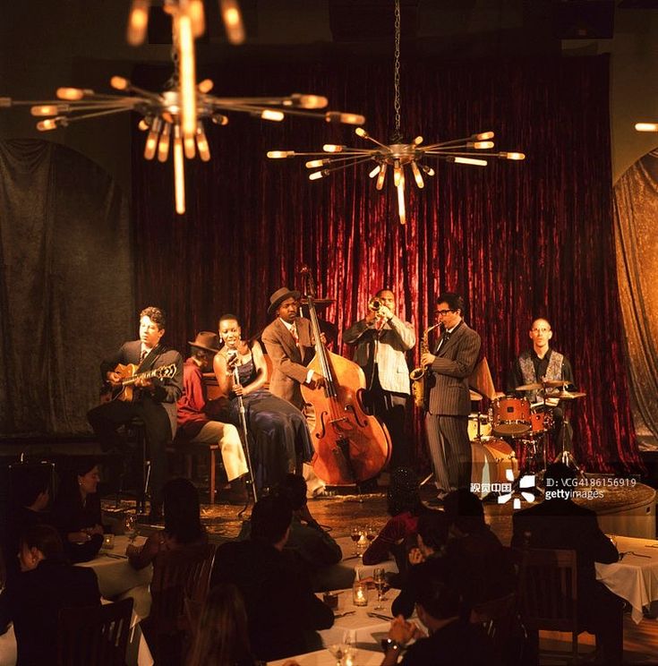 a group of people are playing instruments in a room with red curtains and chandeliers