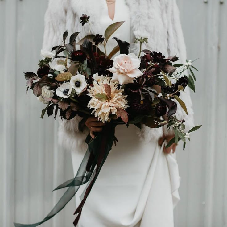 a woman holding a bouquet of flowers in her hand and wearing a fur coat over her shoulders