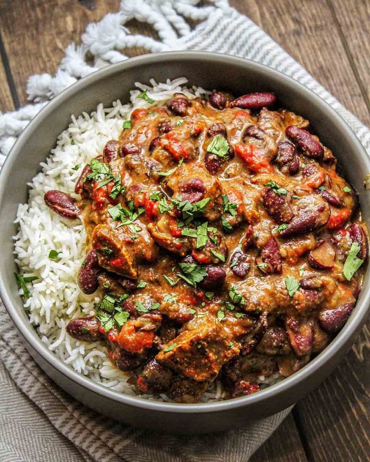 a bowl filled with rice and meat covered in sauce on top of a wooden table