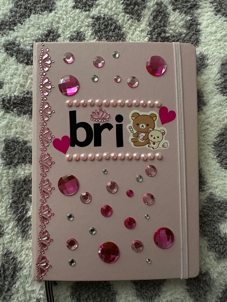 a pink notebook with the word bri written on it, surrounded by hearts and sequins