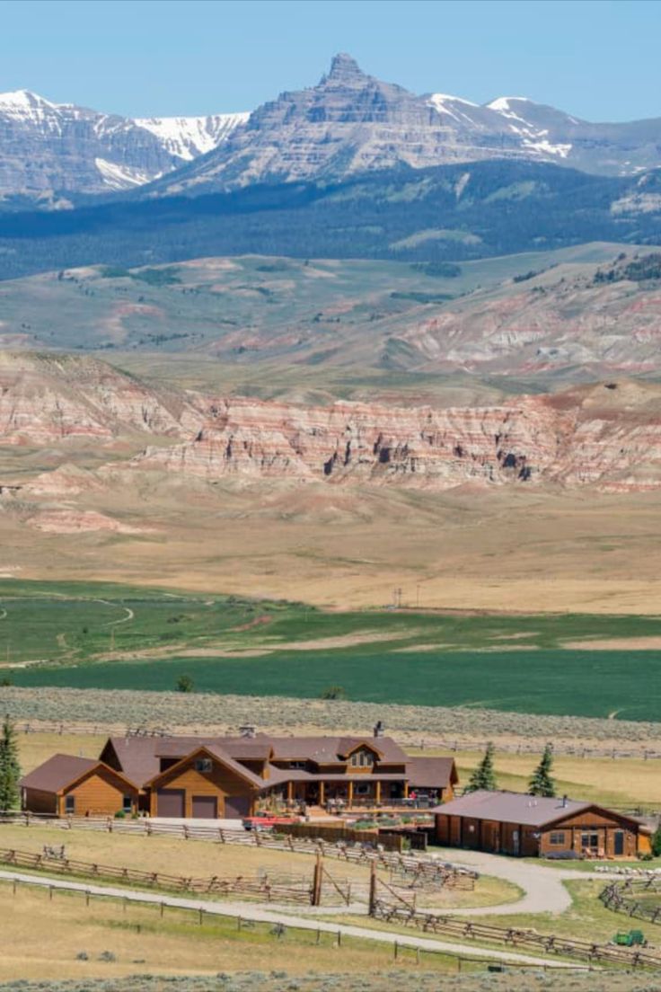 a large house in the middle of a field with mountains in the backgroud