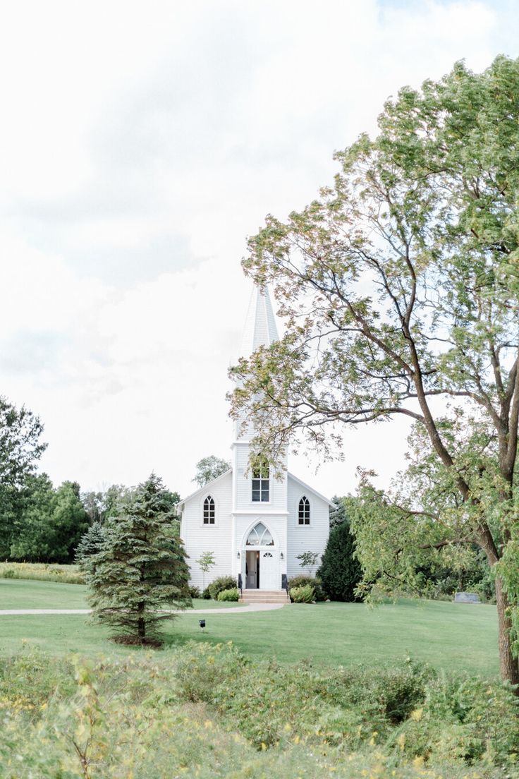 a white church with a tall steeple surrounded by trees