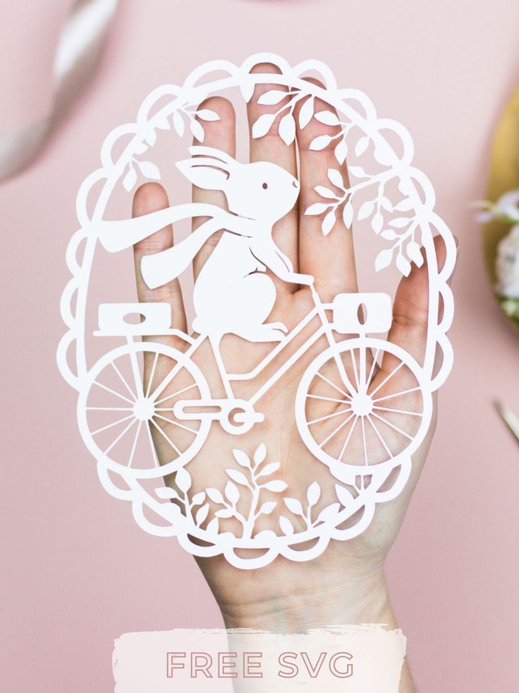 a person holding up a paper cut out of a rabbit on a bike with flowers