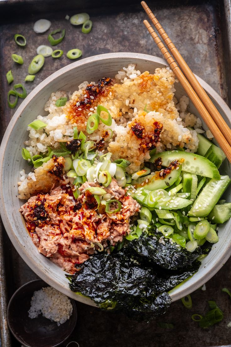 a bowl filled with rice, meat and veggies next to chopsticks