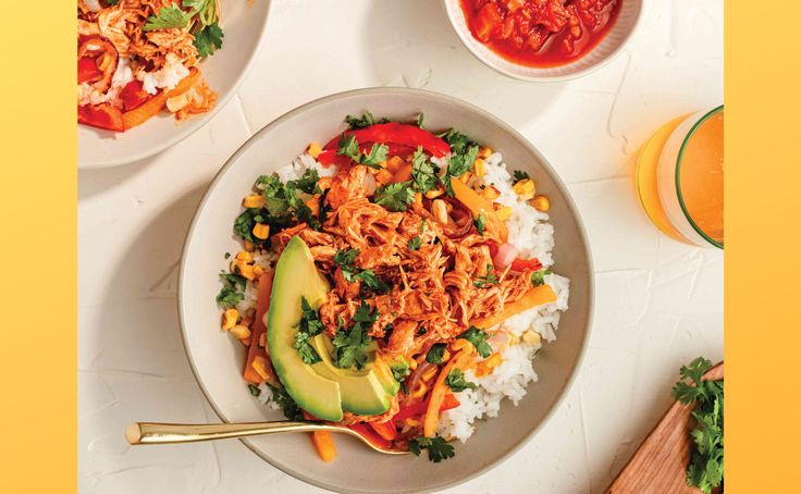 two plates of food with rice, avocado and sauces on the side