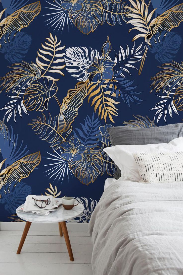 a bedroom with blue and gold wallpaper, white bedding and a plant pattern on the wall