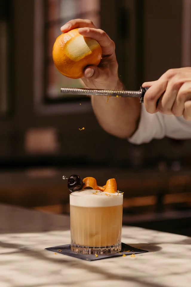 a person holding an orange over a glass filled with liquid