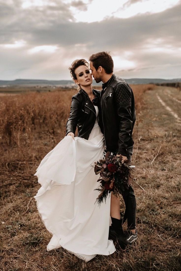 a man and woman in black leather jackets standing next to each other on a field