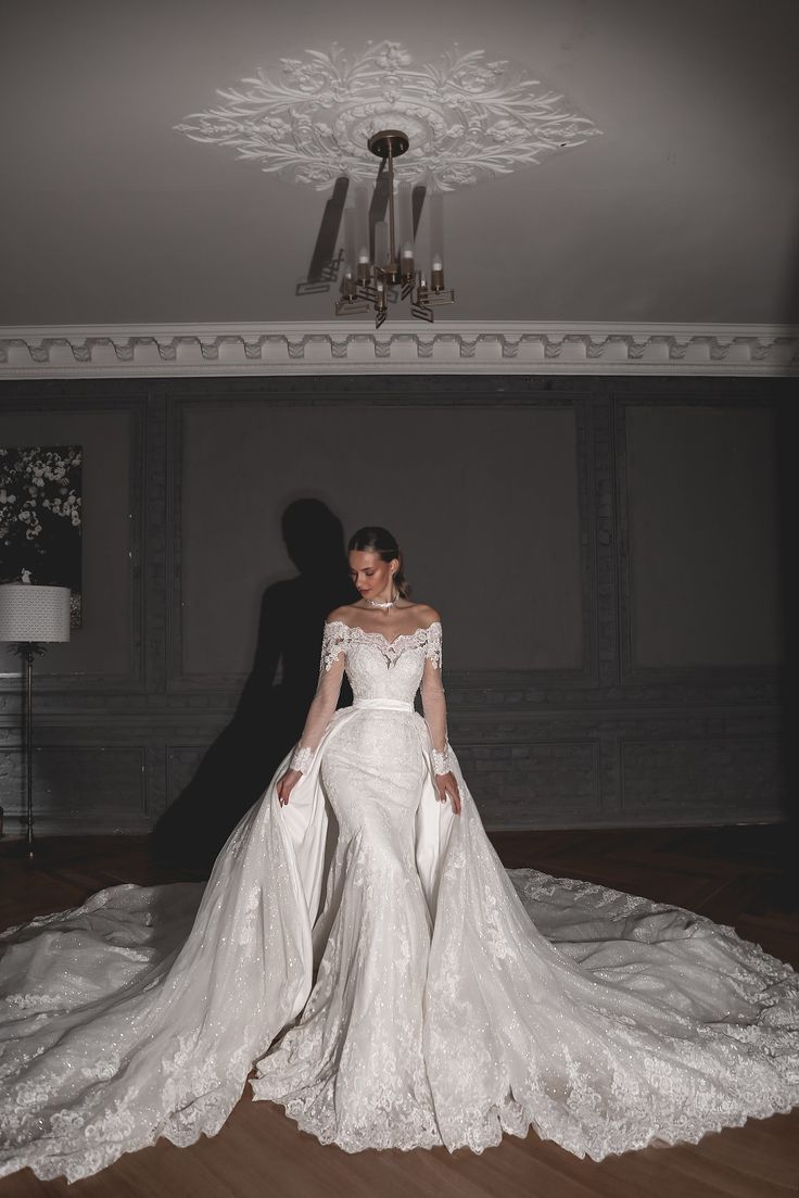 a woman in a white wedding dress standing on a wooden floor with her arms behind her back