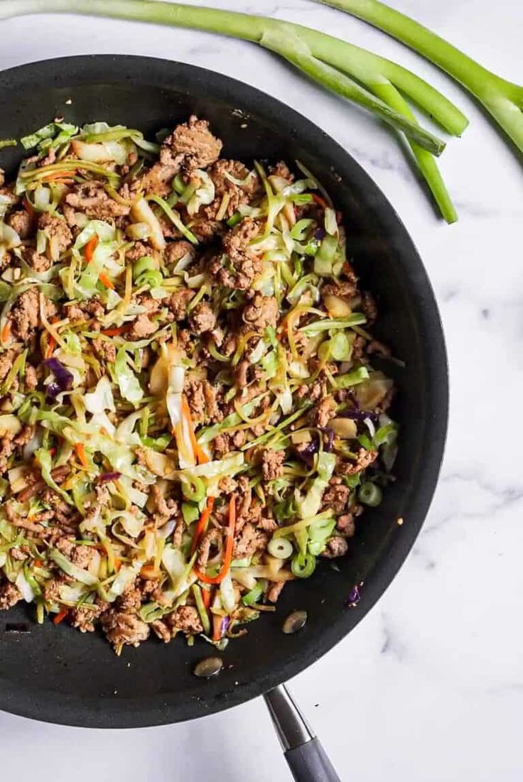 a skillet filled with ground beef, cabbage and carrots