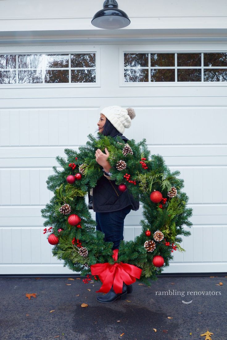 a woman holding a christmas wreath in front of a garage door