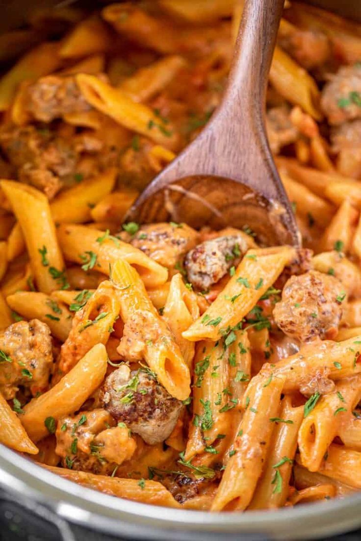 pasta with meatballs and sauce in a slow cooker being stirred by a wooden spoon