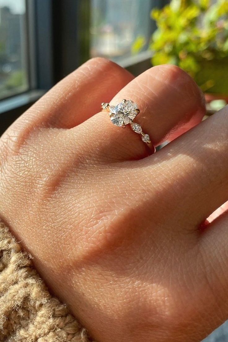 a woman's hand with a diamond ring on top of her finger, in front of a window